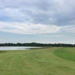 Open grassy area with pond of water and cloudy blue sky